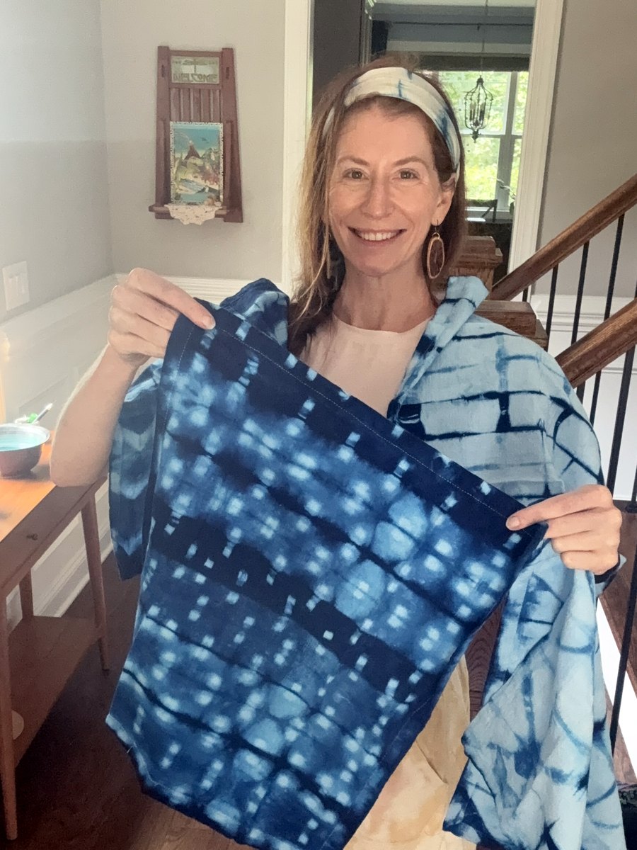 Kristi Thompson holding a deep indigo napkin with rows of white clothespin marks, with a paler shibori napkin over her shoulder